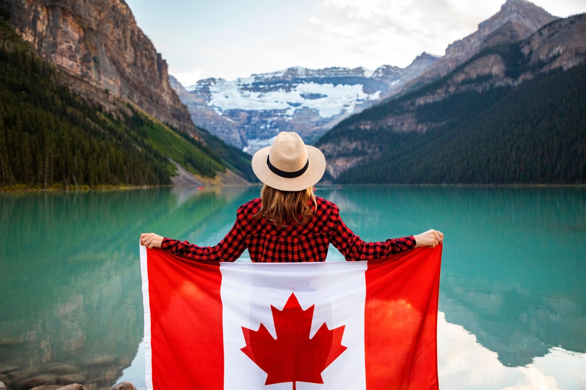 A student in Canada holding a Canadian flag by a mountain lake.
